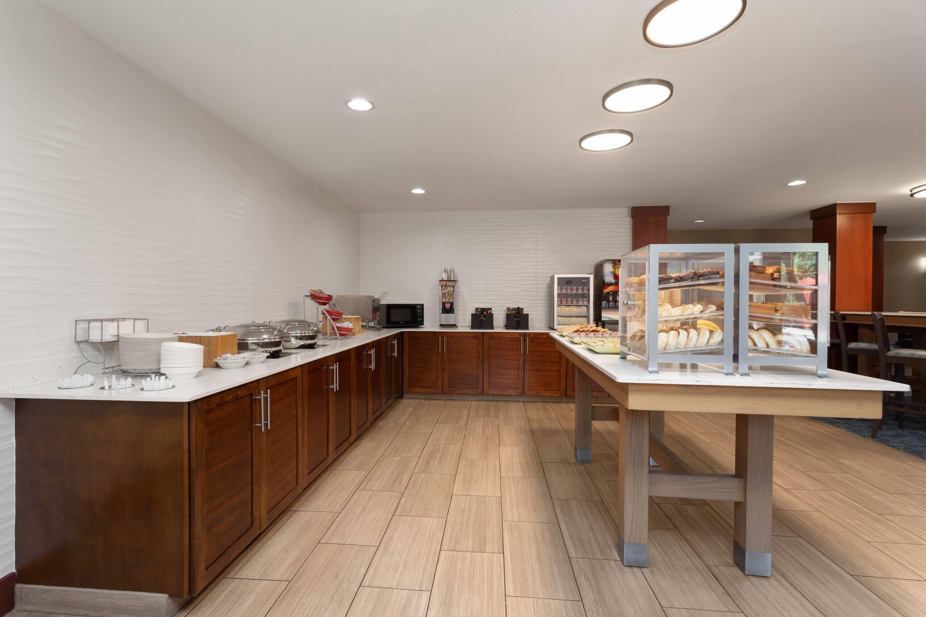 A modern kitchen with wooden cabinets, a white countertop, and a display case with baked goods.