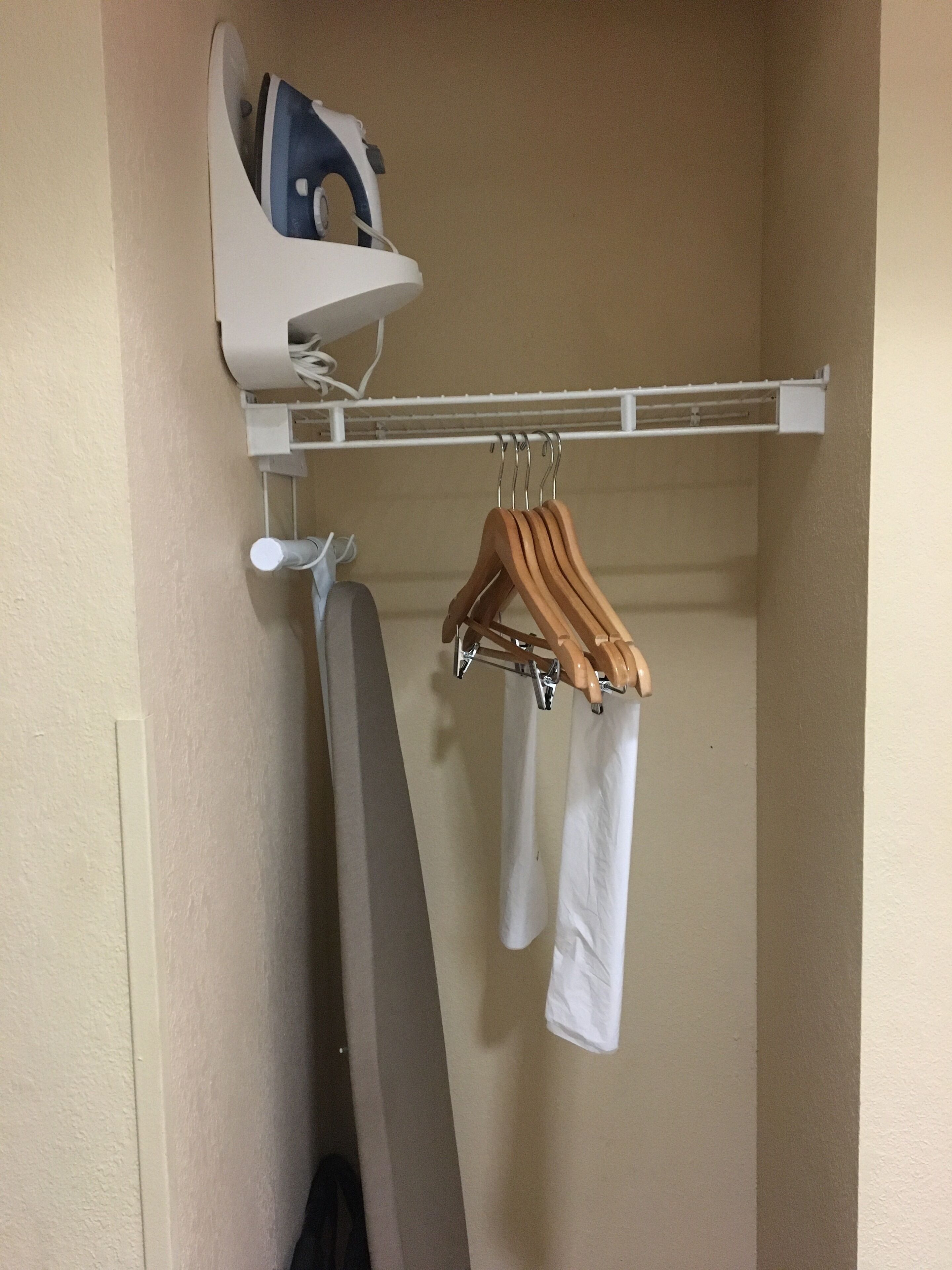 A wall-mounted ironing board with a hanging rack above it, holding several wooden hangers and white garments.
