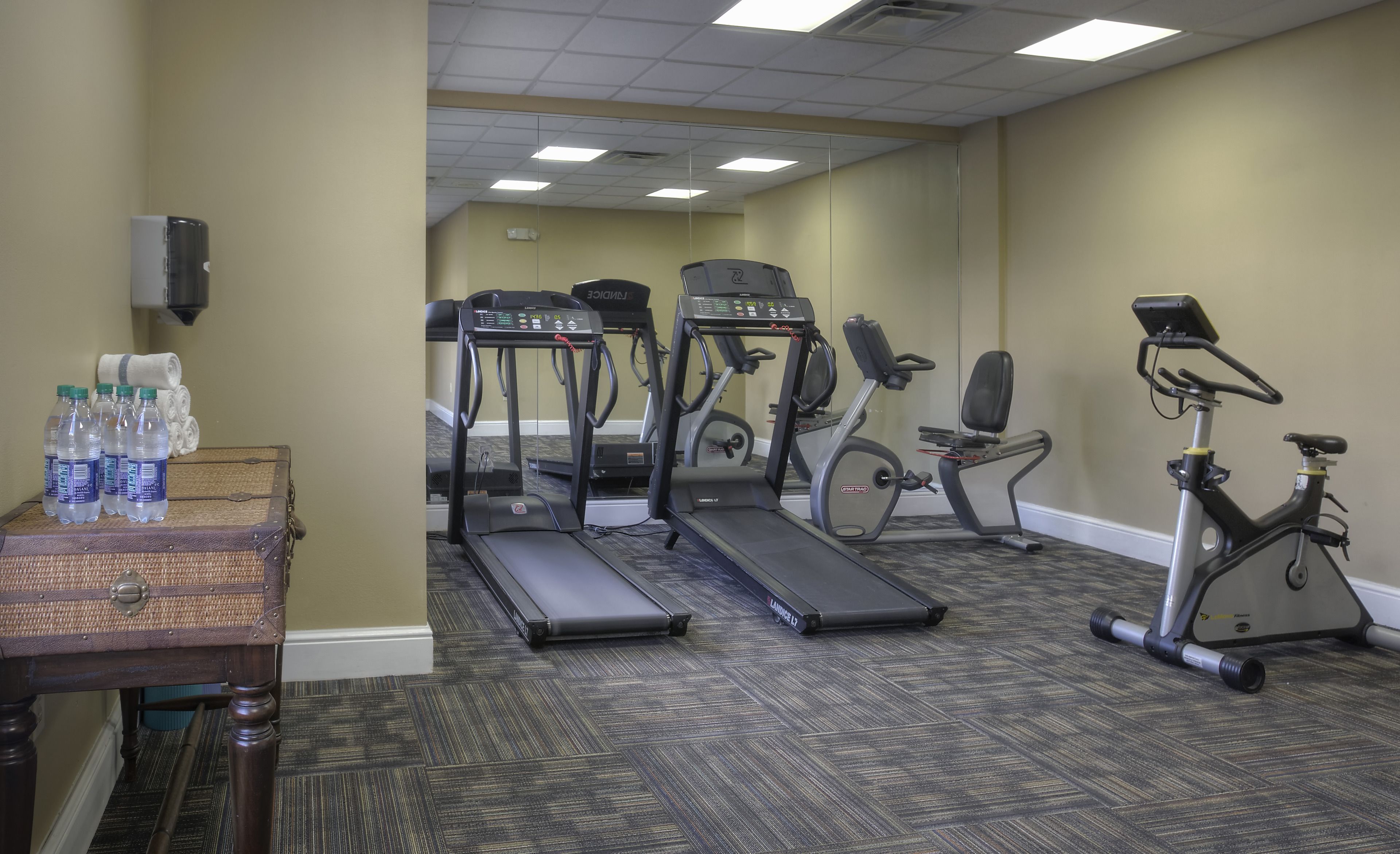 A fitness room with treadmills, an elliptical, and a stationary bike. There are water bottles on a table.