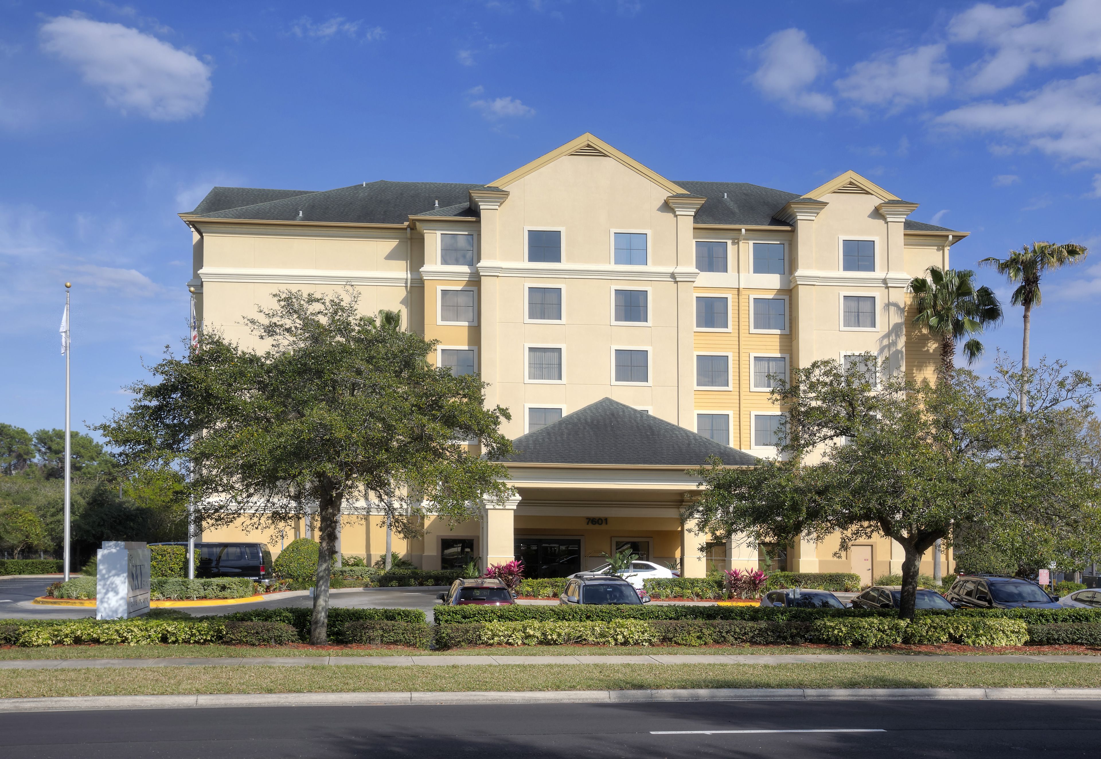 A multi-story hotel with a symmetrical facade, a central entrance, and a parking area in front.