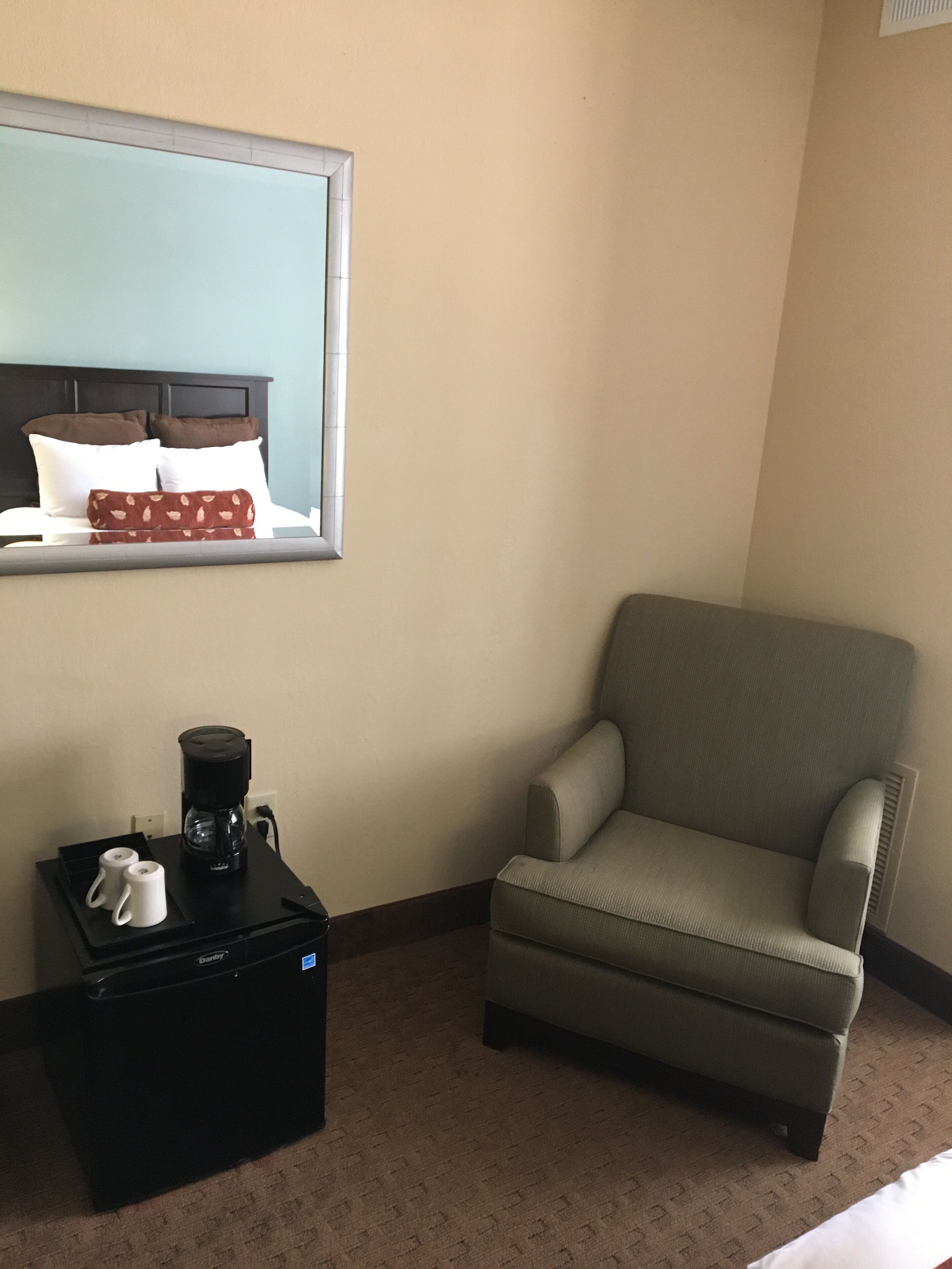 A hotel room with a bed, a chair, a coffee maker, and a window.