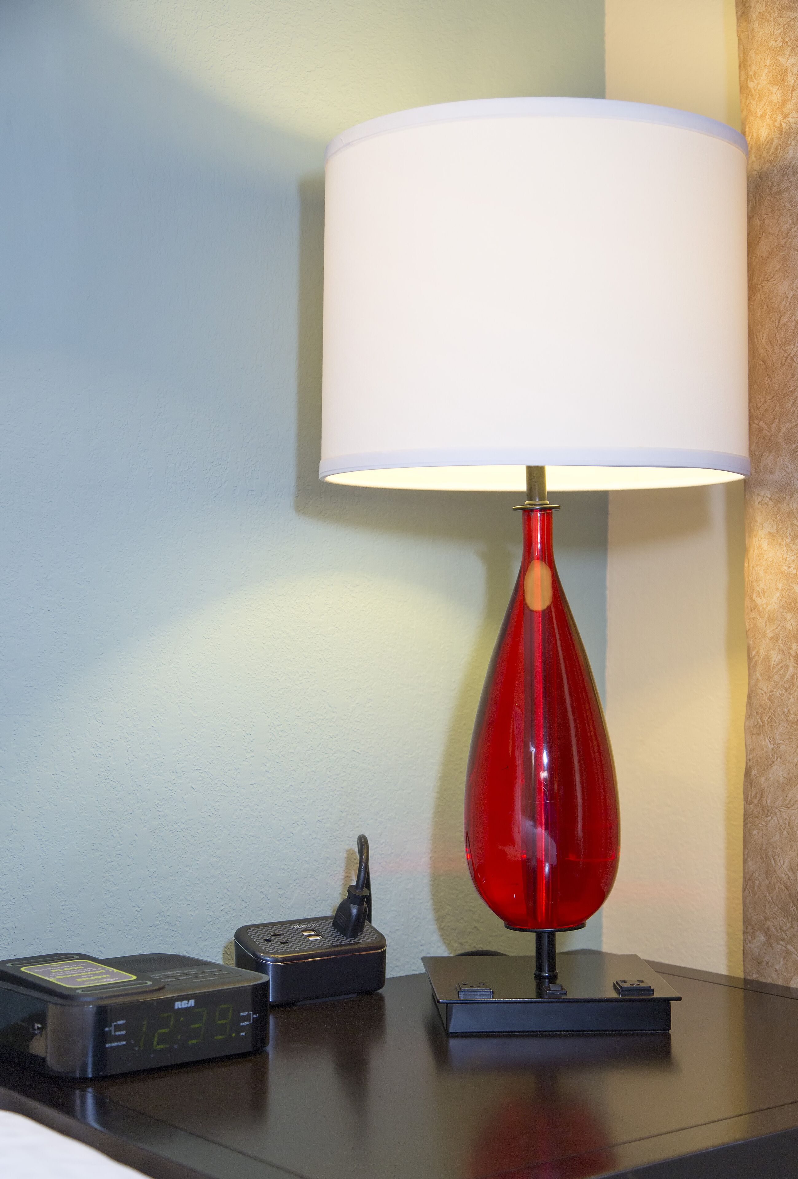 Een tafel met een rode lamp, een klok en een oplader voor een telefoon.