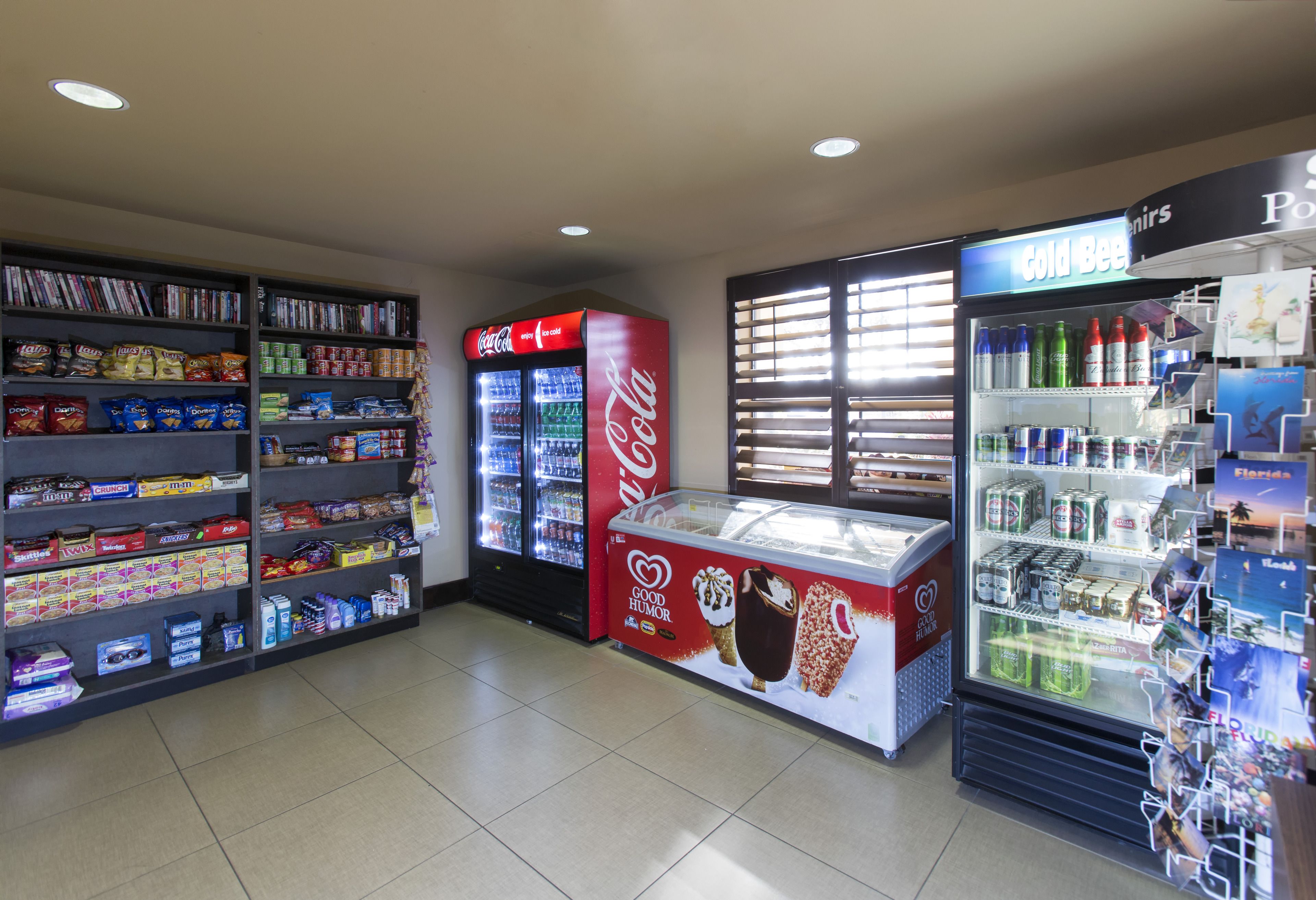 Une épicerie de proximité où les étagères sont remplies de collations, un réfrigérateur rempli de Coca-Cola et un congélateur contenant des glaces.