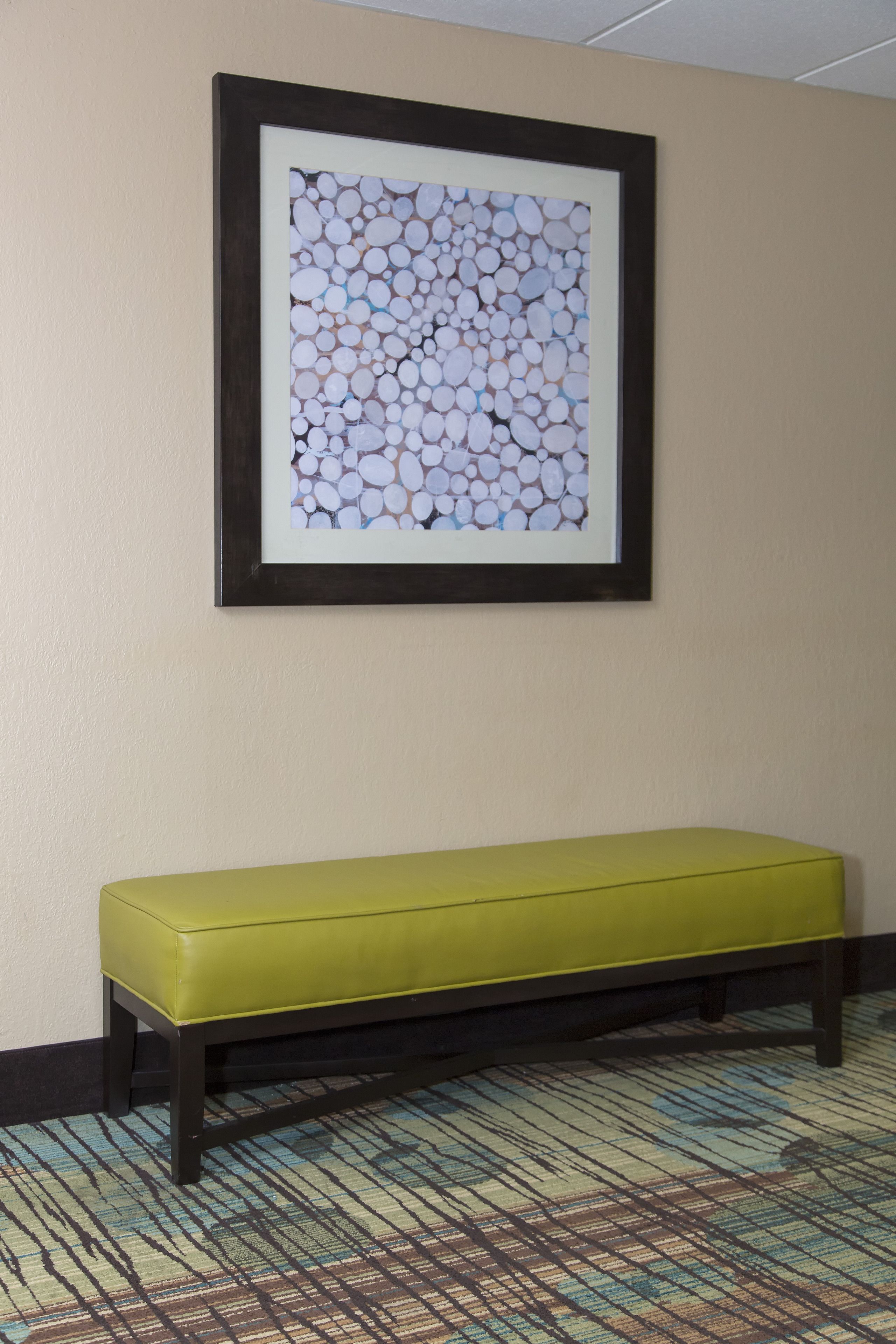 A room with a framed abstract artwork on the wall, a yellow bench, and a patterned carpet.