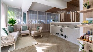 A reception area with wicker furniture, a large potted plant, and a sign for "The Garden Hotel & Resort".