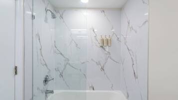 Un bany modern amb dutxa protegida per vidre, paret de marbre blanc i banyera.