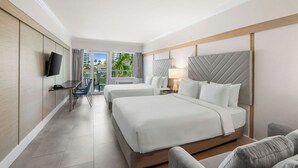 A hotel room with two beds, a desk, a TV, and a view of palm trees.