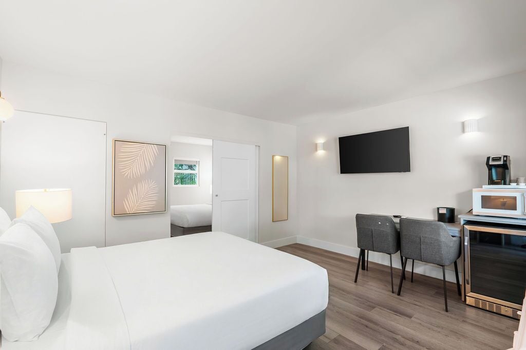 A modern hotel room with a bed, a desk with a chair, a flat-screen TV, a microwave, and a coffee maker.