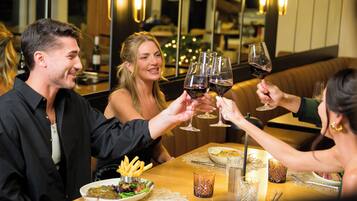 A group of people toasting with wine glasses at a restaurant with a wooden table, plates of food, and a cozy interior.