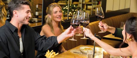 Un groupe de personnes trinquant avec des verres de vin dans un restaurant, autour d’une table en bois, avec des assiettes de nourriture et dans une ambiance chaleureuse.