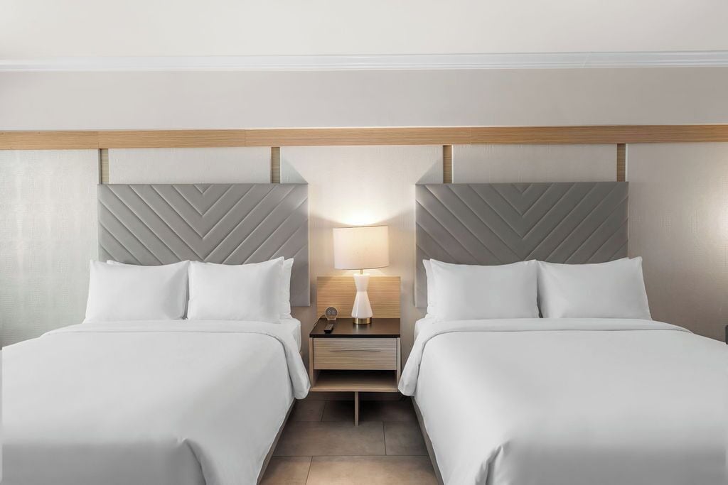 A hotel room with two beds, a nightstand with a lamp, and a wooden headboard.