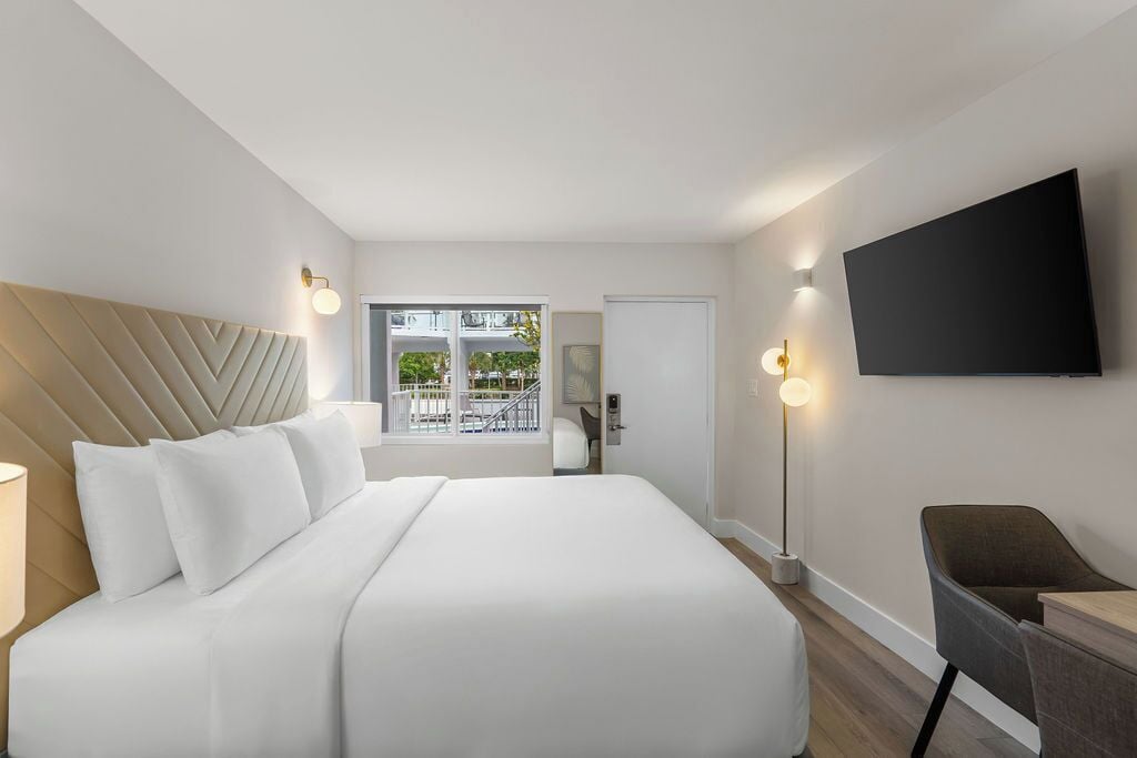 Moderni hotellihuone, jossa on suuri sänky, taulutelevisio, työpöytä ja parveke, jolta on näkymä.
