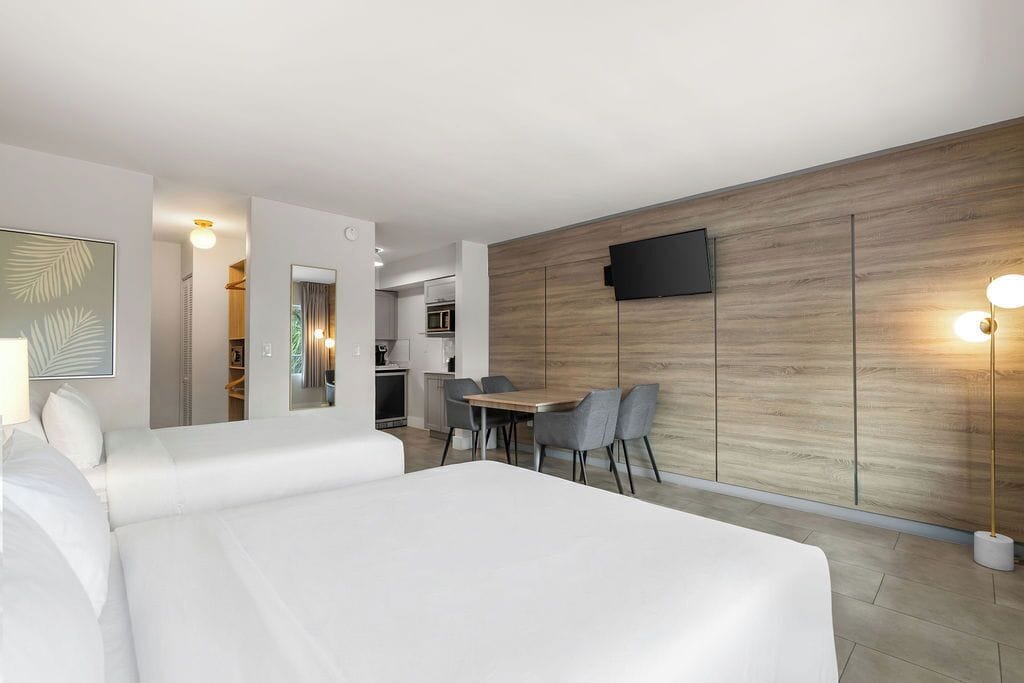 Una habitación de hotel moderna con una cama grande, un área de comedor con sillas, un televisor montado en la pared y una pared de acento de madera.