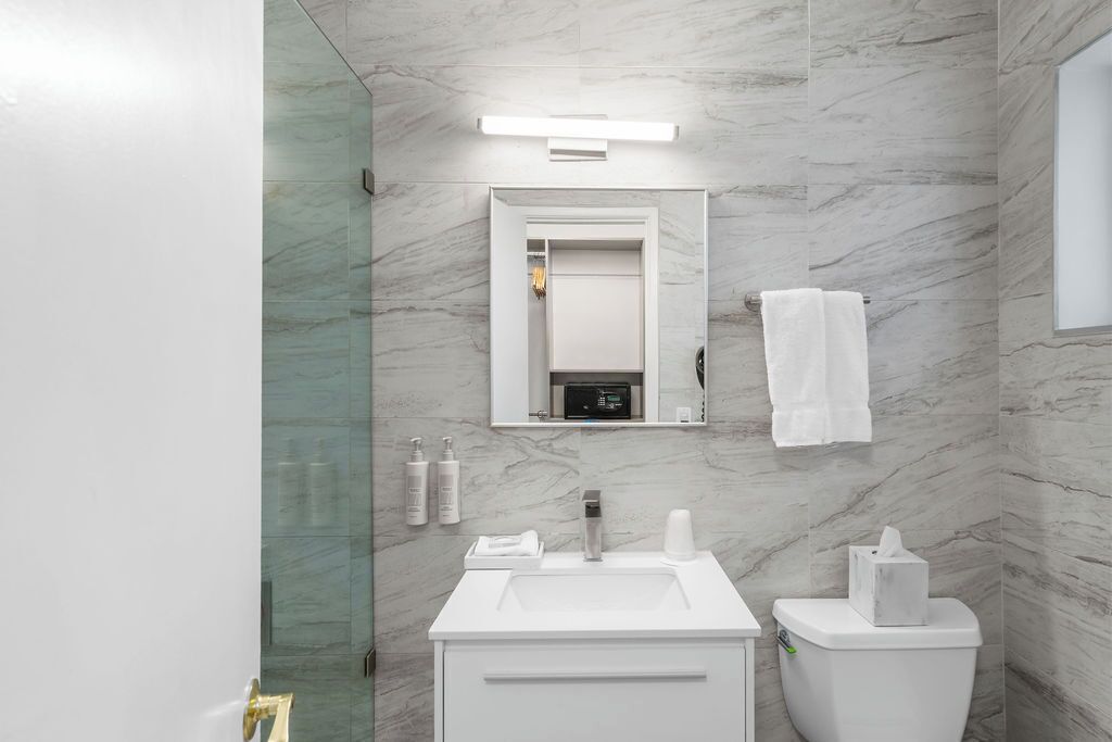 Un baño moderno con pared de mármol, un lavamanos, un inodoro, un espejo y un perchero para toallas.
