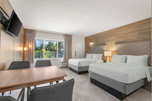 Une chambre d’hôtel avec une tête de lit en bois, un grand lit, un plus petit lit, un bureau et un téléviseur fixé au mur.