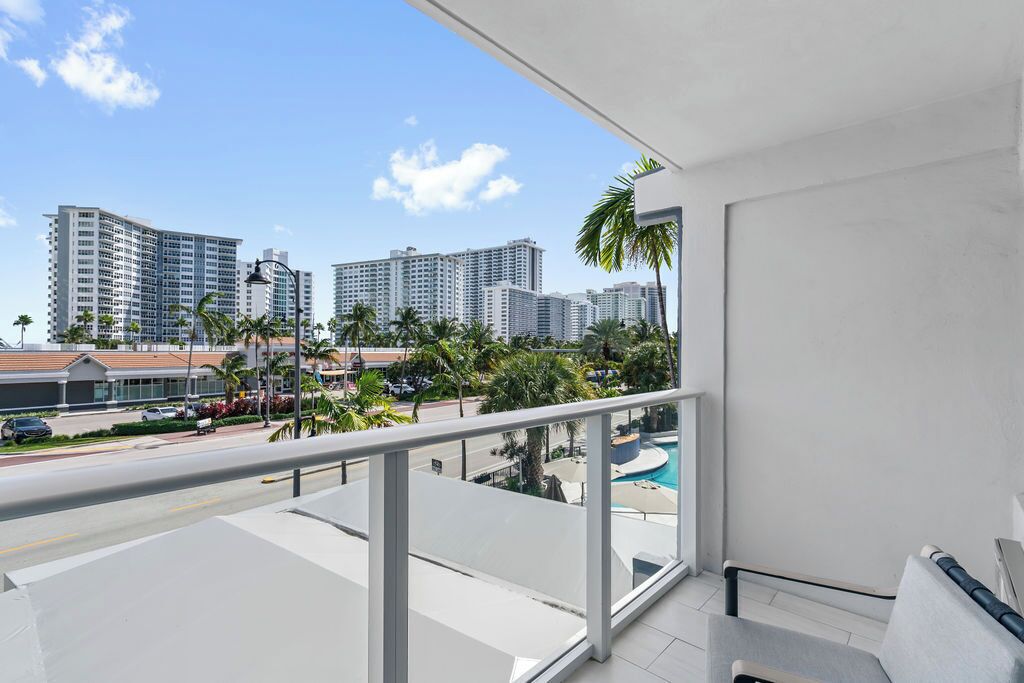 A balcony with a view of high-rise buildings, a swimming pool, and palm trees.