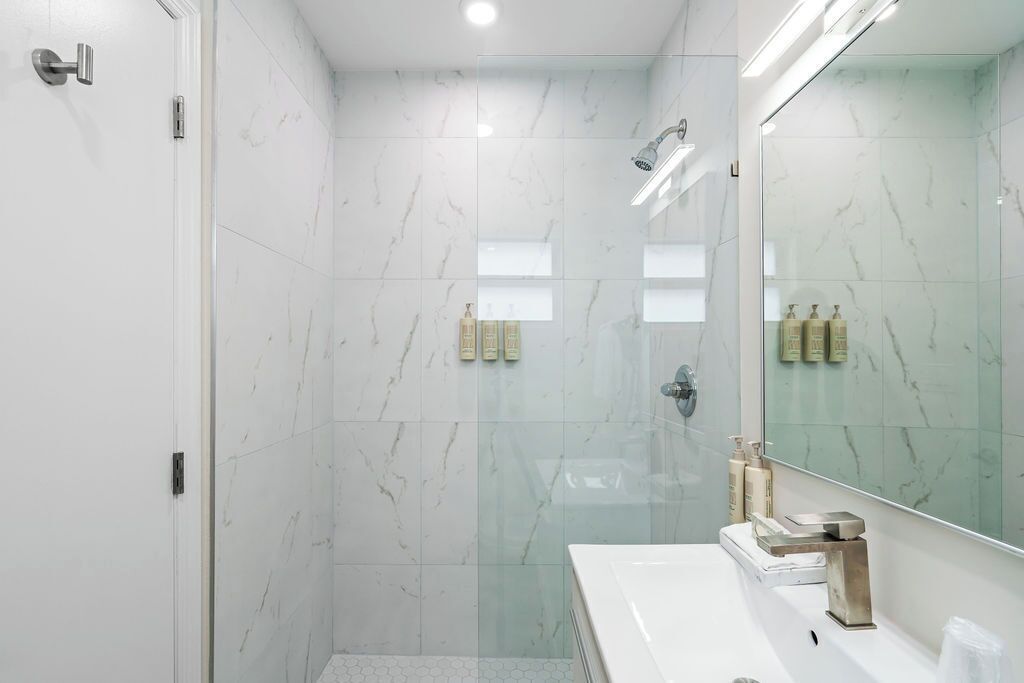 A modern bathroom with a glass-enclosed shower, a white sink, and a large mirror.