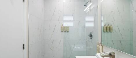 A modern bathroom with a glass-enclosed shower, a white sink, and a large mirror.