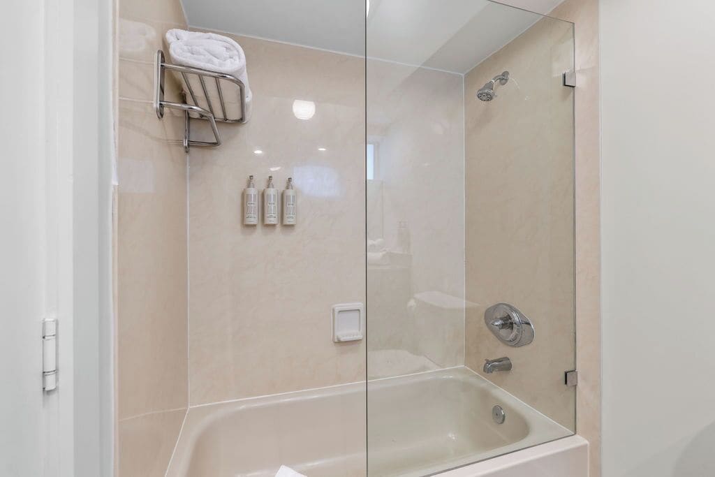 A modern bathroom with a glass-enclosed shower, a white bathtub, and a towel rack with folded towels.
