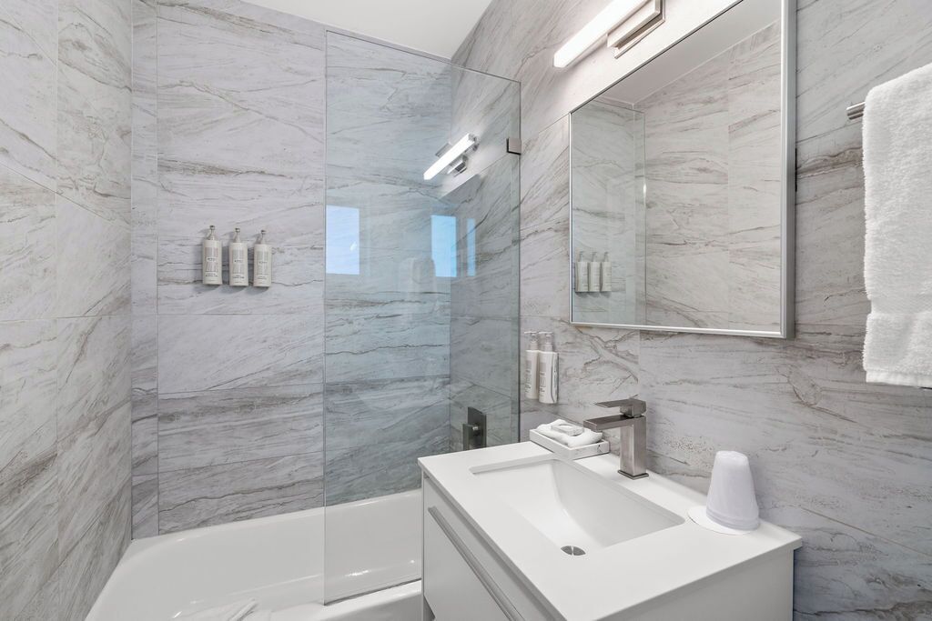 A modern bathroom with a glass shower enclosure, a white sink, and a large mirror.
