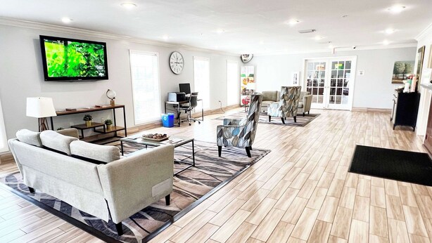 A modern living room with a sofa, coffee table, and TV. There is a desk with a computer and a chair. The room has wooden flooring and a patterned rug. - Quality Inn Gainesville I-75 (Gainesville)
