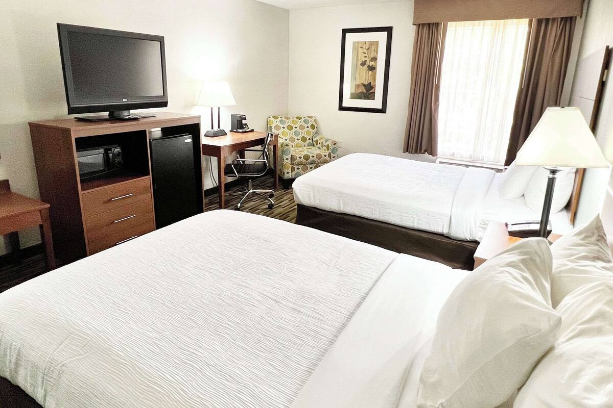 A hotel room with two beds, a desk with a computer, a television, and a chair.