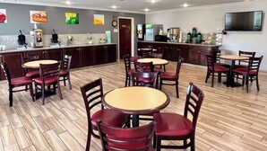 A restaurant with multiple tables and chairs, a kitchen area with appliances, and a flat-screen TV mounted on the wall. - Quality Inn Gainesville I-75 (Gainesville)
