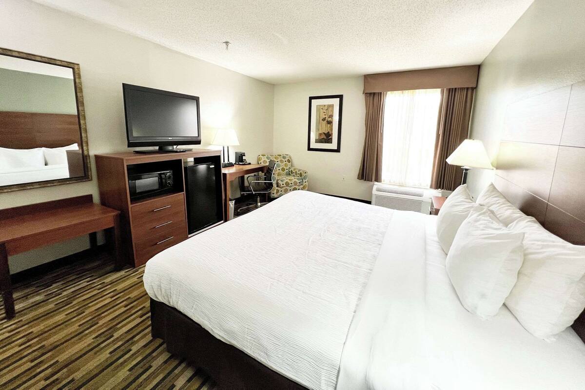 A hotel room with a large bed, a desk with a television, a chair, and a window with curtains.