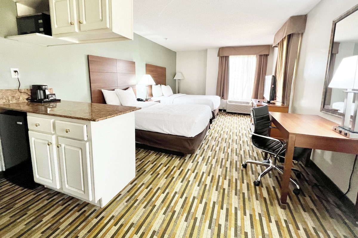 A hotel room with a bed, a desk, a chair, a desk lamp, a coffee maker, and a TV.