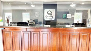 A reception desk with a glass partition, a clock, and a sign for 'Quality by Choice Hotels'. - Quality Inn Gainesville I-75 (Gainesville)