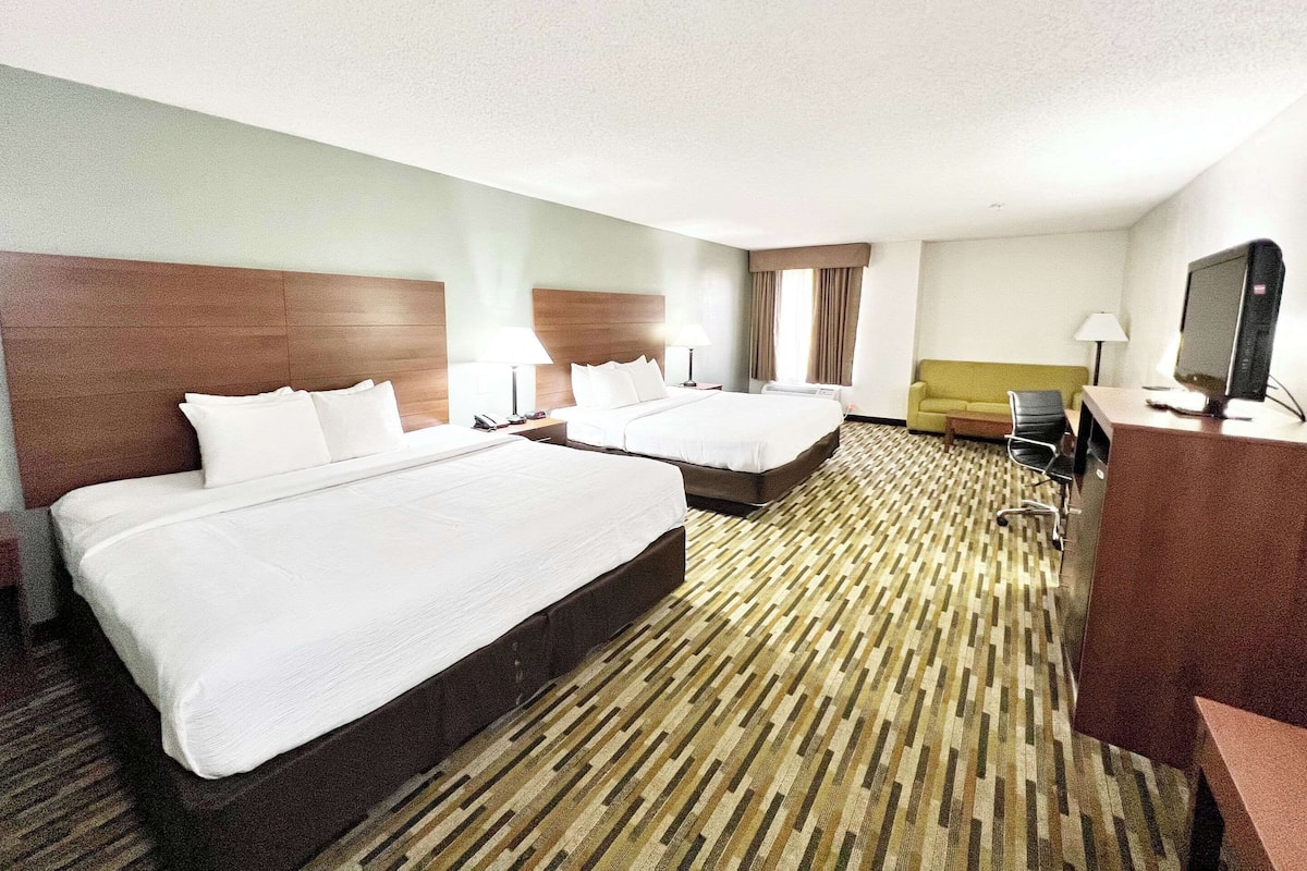 A hotel room with two beds, a desk with a computer, a sofa, and a TV.