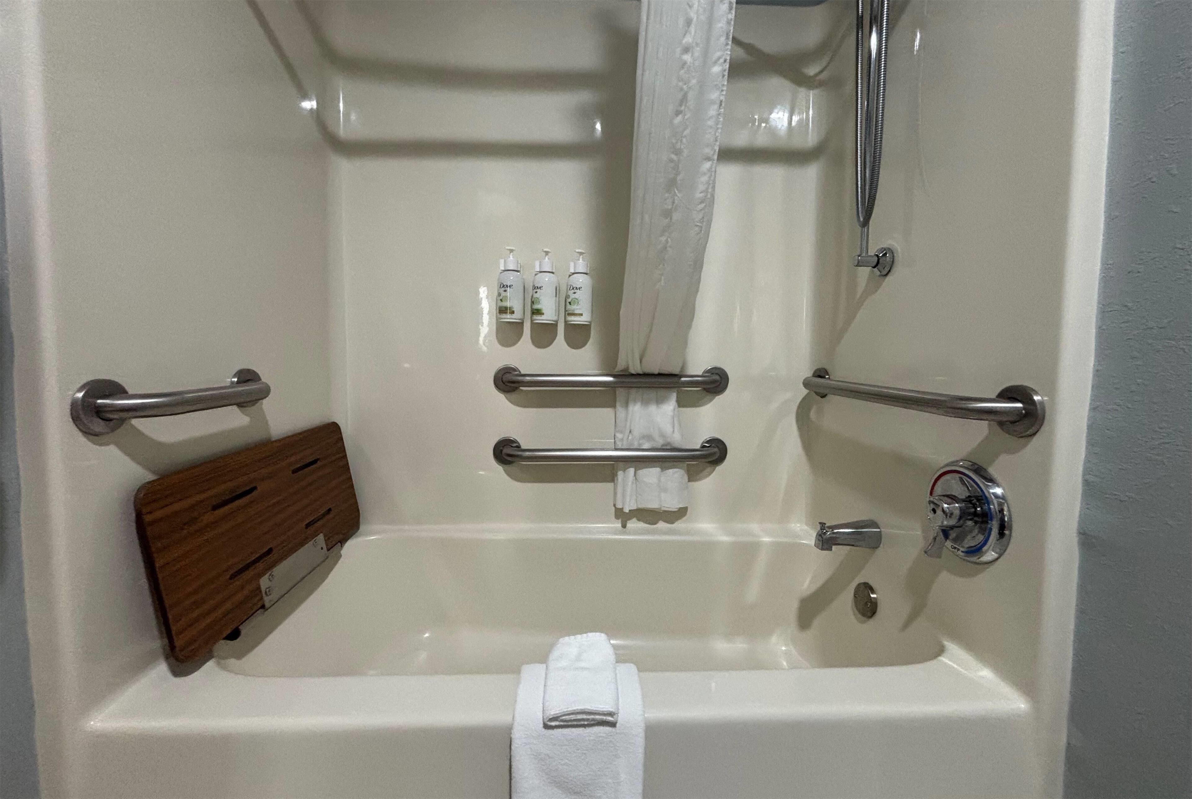 A bathtub with a wooden tray, a towel, and three bottles of shampoo.