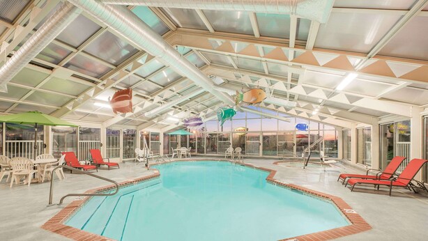 An indoor swimming pool with a clear view of the sky through the roof, surrounded by red lounge chairs and a few tables. - Baymont by Wyndham Litchfield (Litchfield)