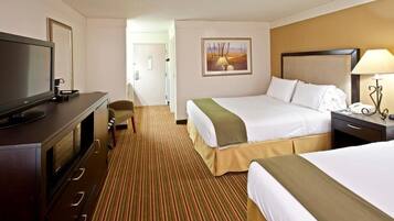 A hotel room with a large bed, a smaller bed, a television, a desk with a lamp, and a painting on the wall.
