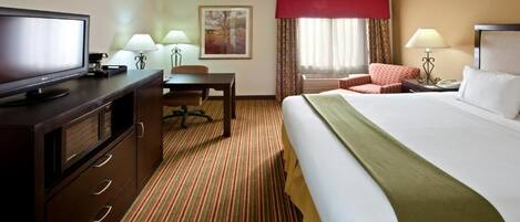 A hotel room with a bed, desk, chair, television, lamps, and a painting on the wall.