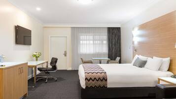 Quarto de hotel com cama, escrivaninha, cadeira e televisão na parede.