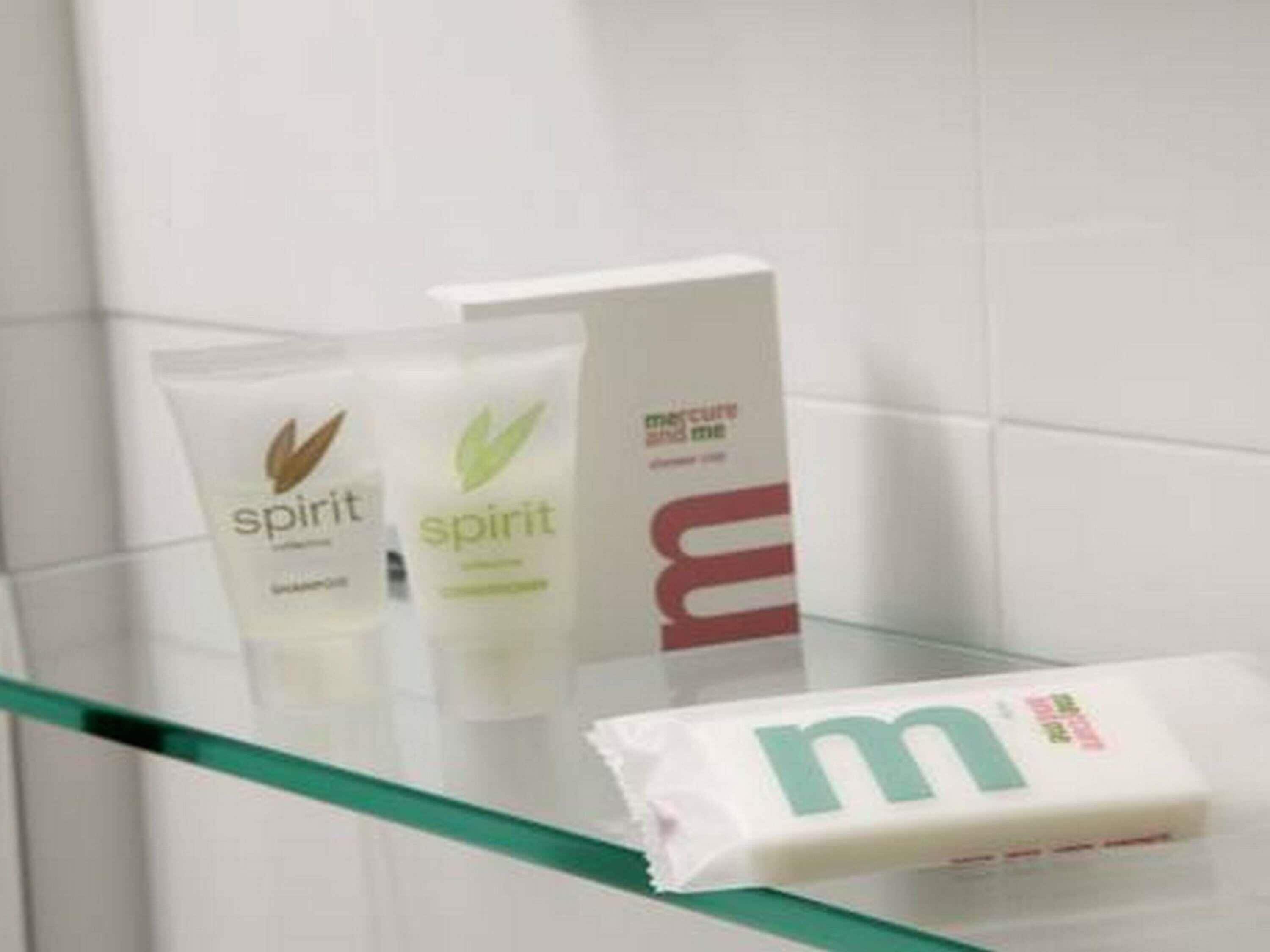 Een badkamer met een douchecabine van glas, een witte handdoek en twee flesjes 'Spirit' shampoo.