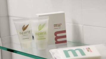 Een badkamer met een douchecabine van glas, een witte handdoek en twee flesjes 'Spirit' shampoo.
