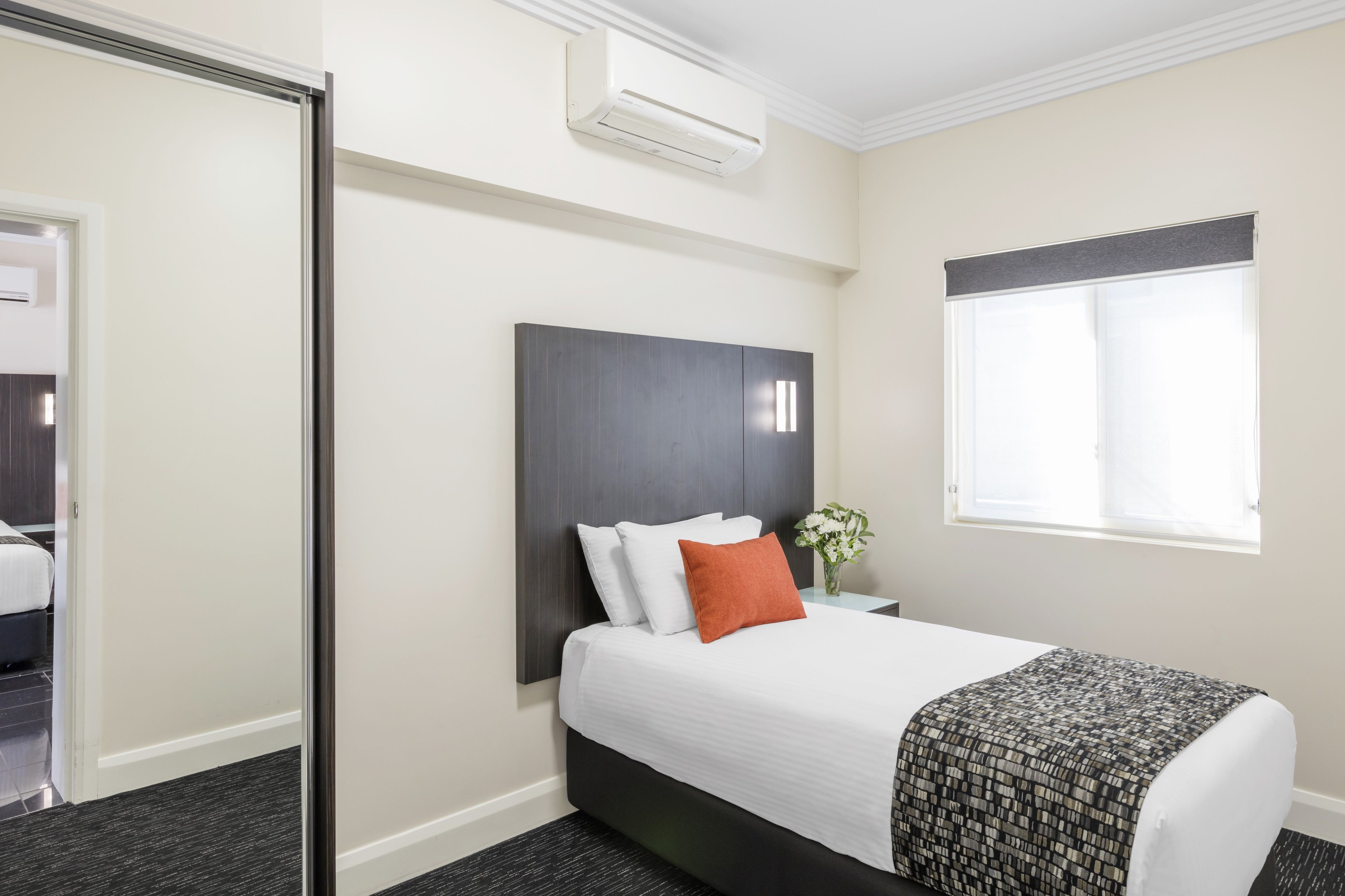 A hotel room with a bed, a nightstand, a window, and an air conditioning unit.