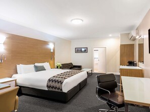 Habitación de hotel con cama, mesita de noche, silla, escritorio y espejo.