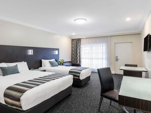 Habitación de hotel con dos camas, un escritorio, una silla, un televisor y una ventana con cortinas.