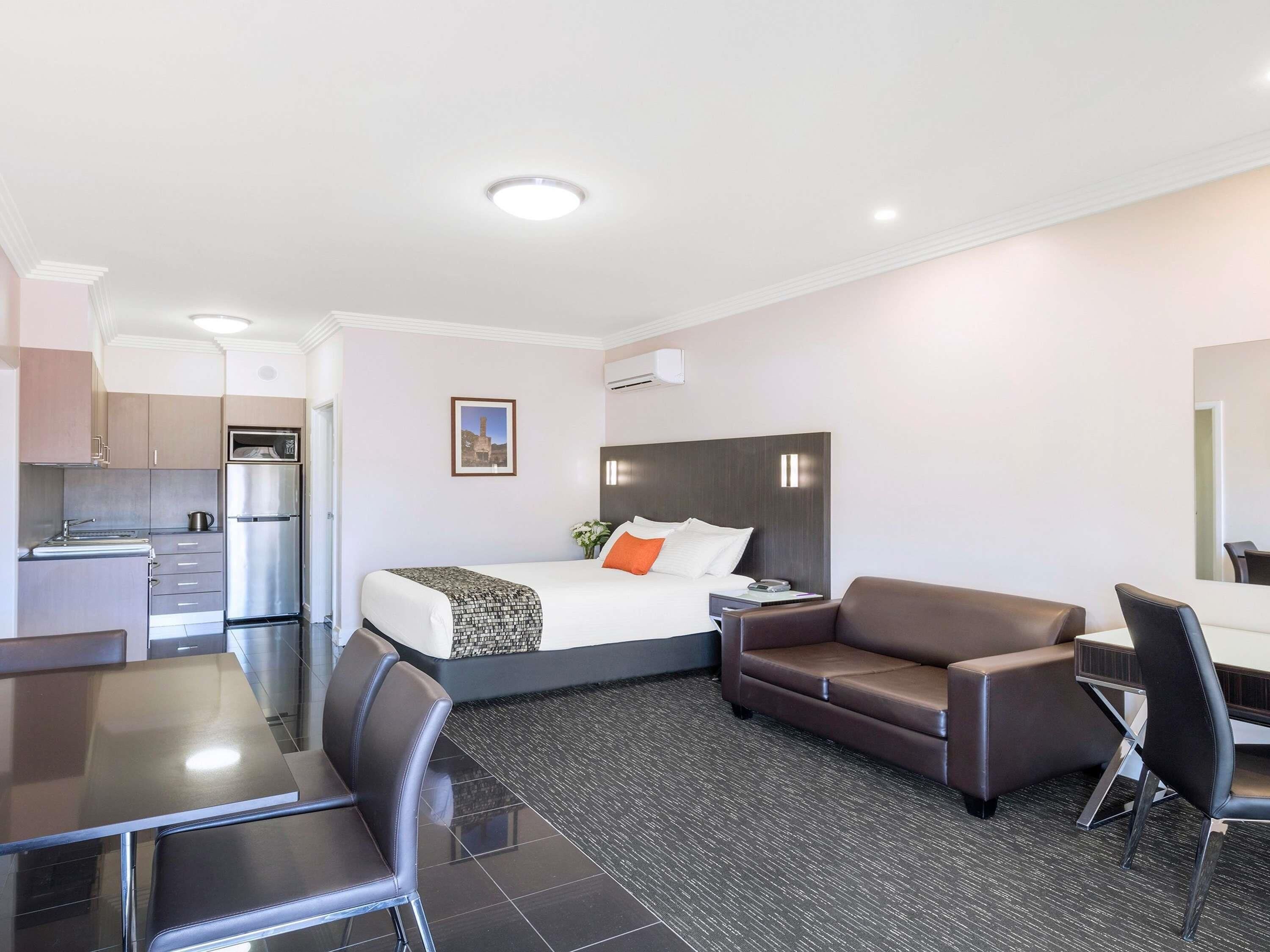 A hotel room with a bed, a sofa, a desk, a chair, a kitchenette, and a bathroom.
