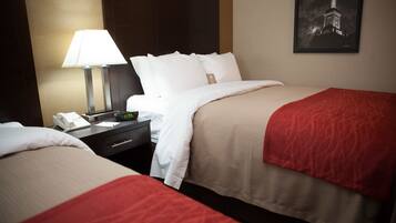 A hotel room with two beds, a nightstand with a lamp, a phone, and a framed picture on the wall.