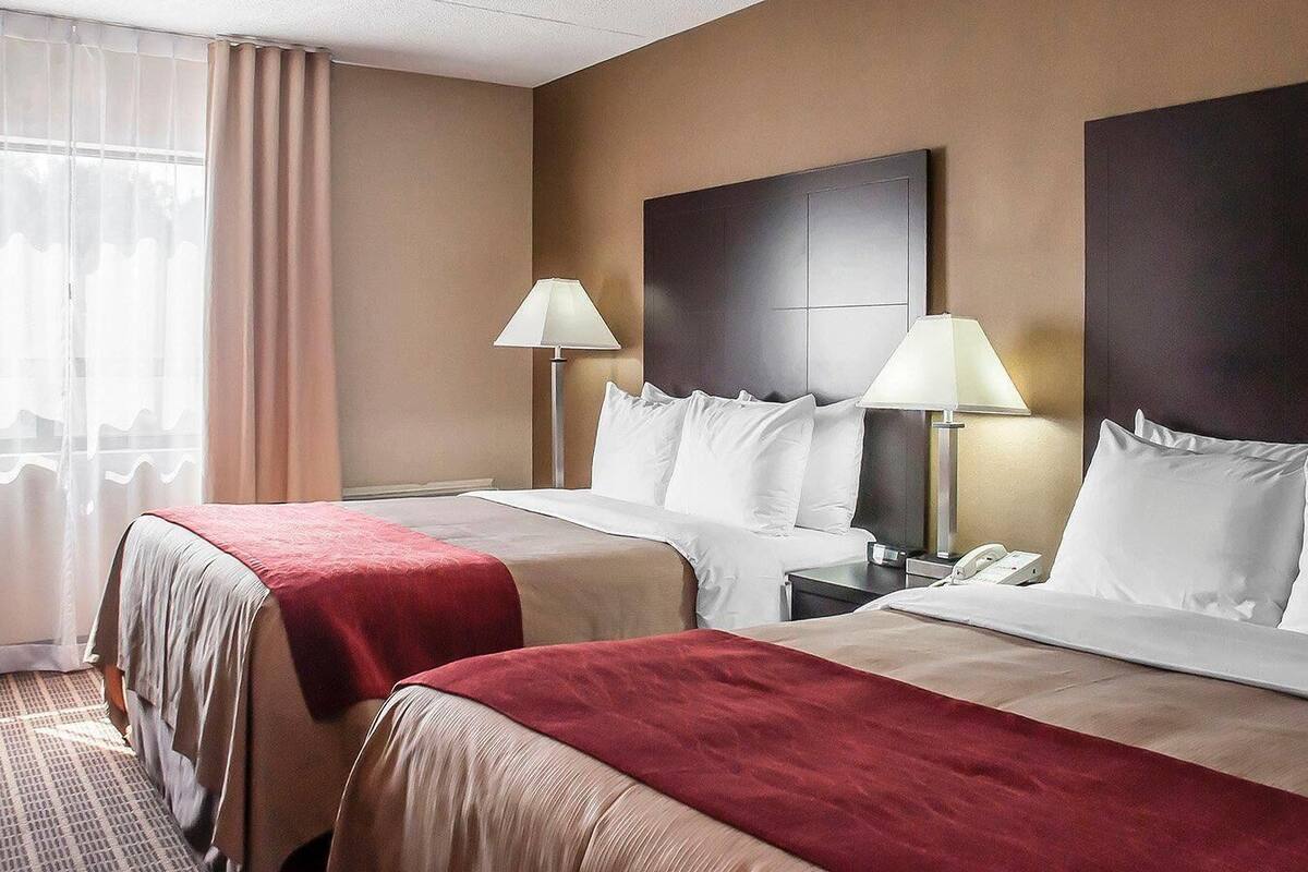 A hotel room with two beds, a large window with curtains, and bedside lamps.