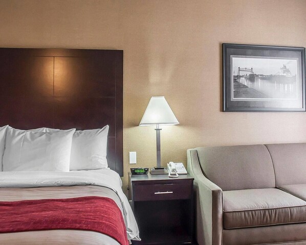 Ein Hotelzimmer mit einem Bett, einem Nachttisch mit Lampe, einem Sessel und einem gerahmten Bild an der Wand.
