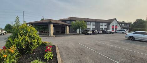 A parking lot with several cars, a building with a covered entrance, and a landscaped area with plants and flowers.
