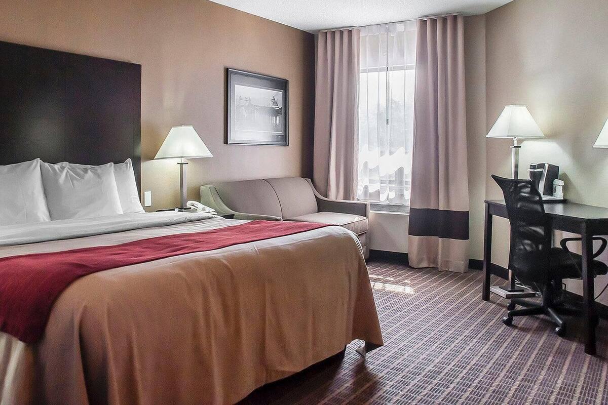 A hotel room with a bed, desk, chair, lamp, and a framed picture on the wall.