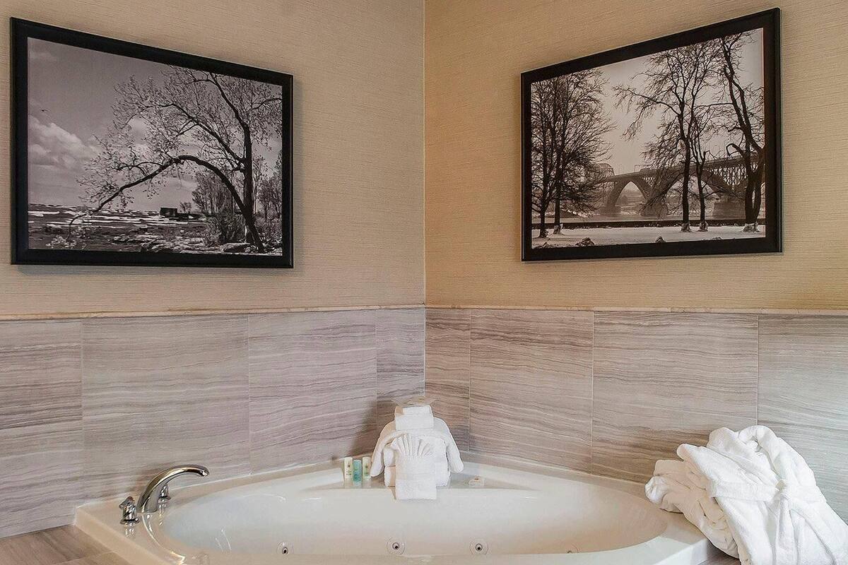 A bathroom with a large bathtub, two framed pictures on the walls, and a towel rack with towels.