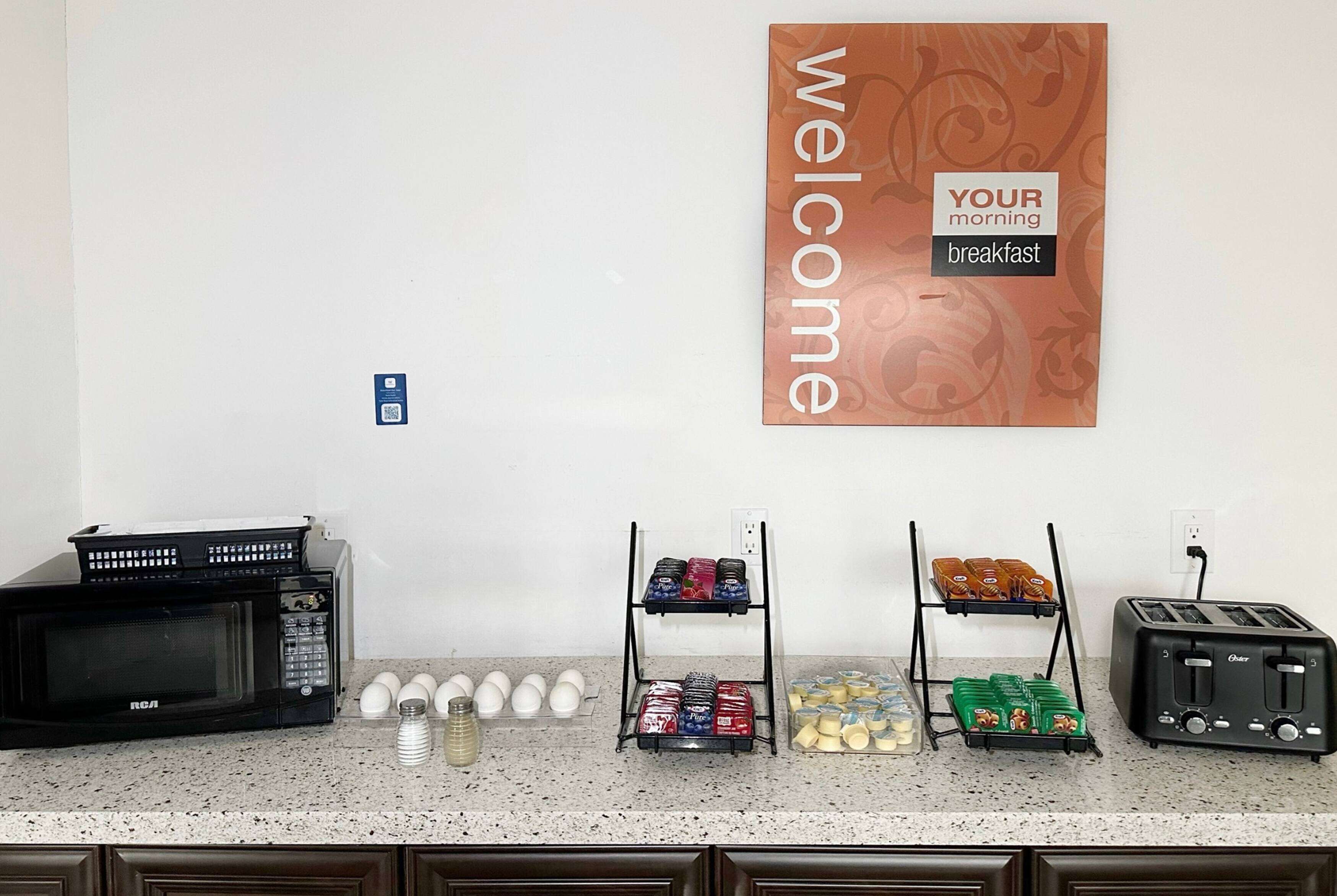 A kitchen counter with a microwave, toaster, and egg carton. There are also shelves with various food items and a welcome sign.