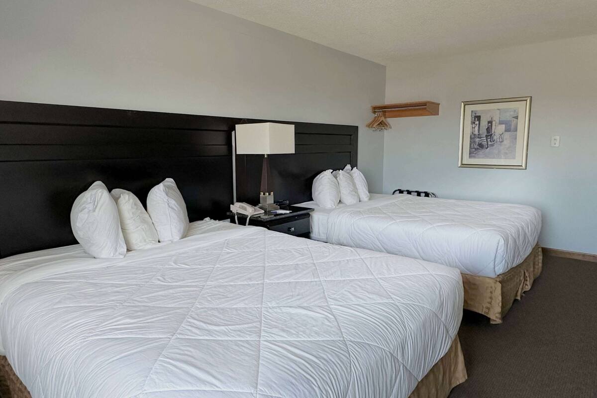 Habitación de hotel con dos camas, una mesita de noche con una lámpara y un cuadro en la pared.